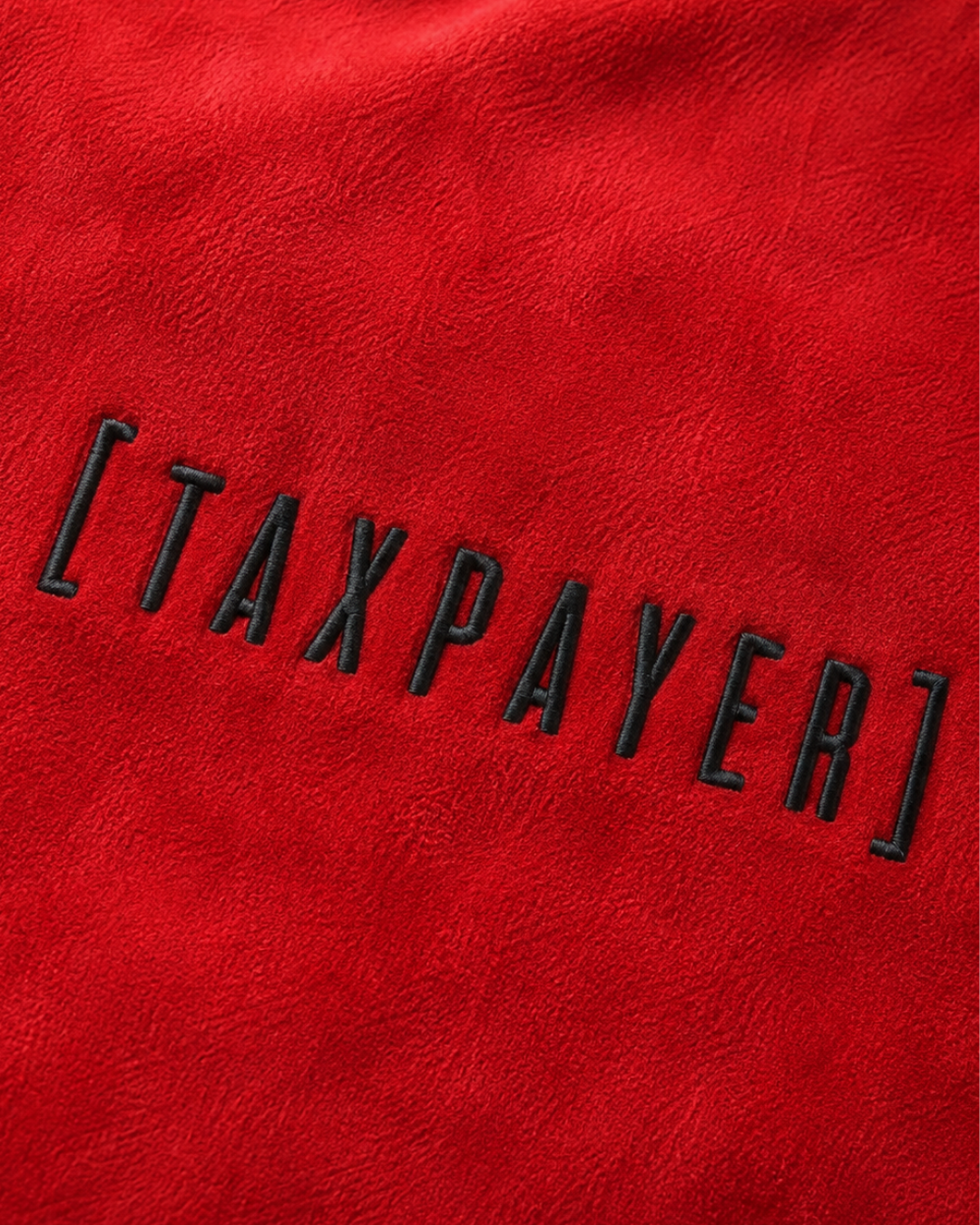 A close-up of a red textured fabric with the word "[TAXPAYER]" embroidered in black outlined letters across the center.